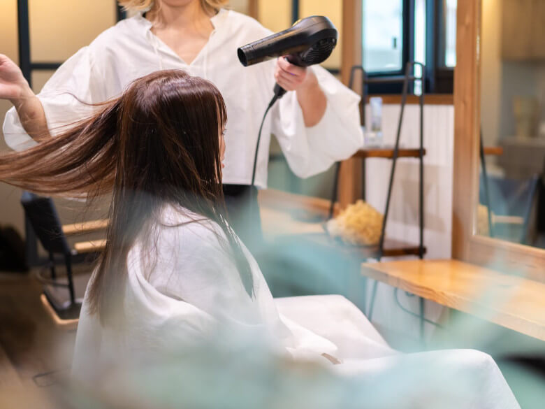 美容室で髪を乾かしてもらう女性